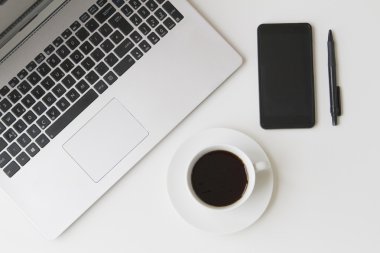 Dizüstü bilgisayar, cep telefonu, kalem ve kahve beyaz masada. Üstten Görünüm. Düz yatıyordu.