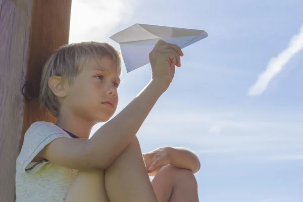 Rapaz a pilotar um avião de papel contra o céu azul. Dia de verão. Vista de ângulo baixo — Fotografia de Stock