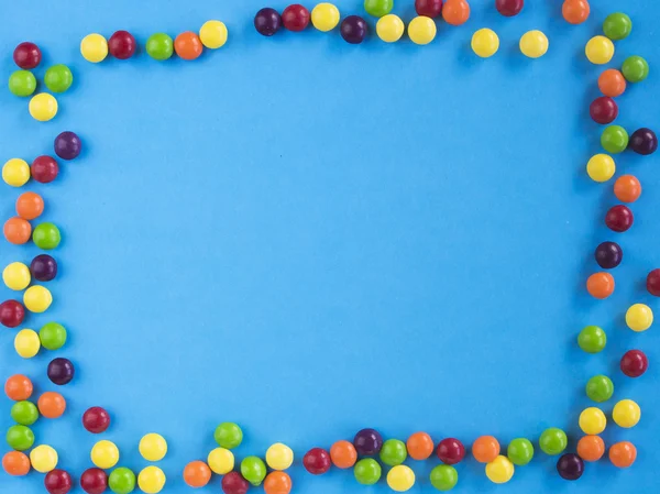 Frame of multicolored small candie on blue background. Copy space for text. Flat lay. Top view — Stock Photo, Image