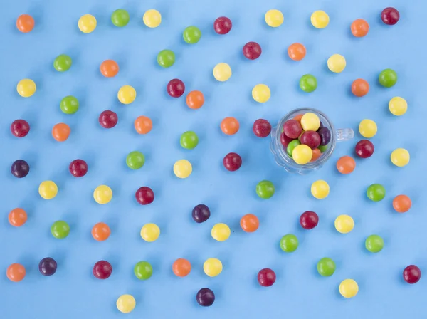 Colorful candies on the blue background and little glass jar with them. Top view. Flat lay — Stock Photo, Image