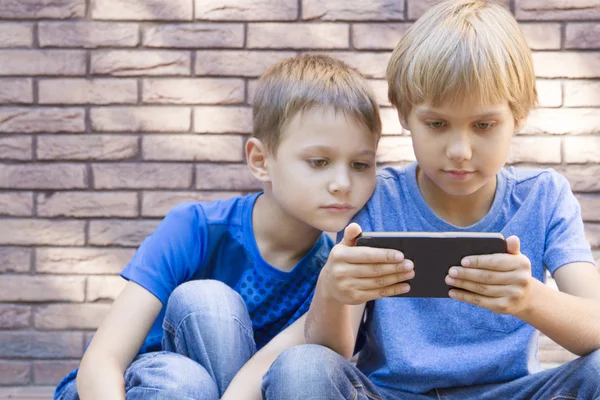 Crianças com telefone celular. Dois meninos olhando para a tela, jogando jogos ou usando o aplicativo. Ao ar livre. Tecnologia educação lazer pessoas amizade conceito — Fotografia de Stock