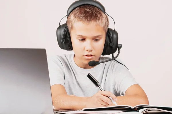 Ragazzo con le cuffie che fa i compiti con il computer portatile. Apprendimento online, istruzione a distanza a casa — Foto Stock