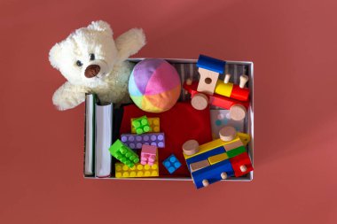 İçinde oyuncaklar, kitaplar, pembe arka planda yardım amaçlı kıyafetler olan bağış kutusu. Üst görünüm