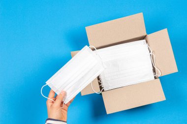 Açık karton kutudan açık mavi arka planda bir sürü tıbbi maskesi olan bir tıbbi maskeyi almak. Üst görünüm