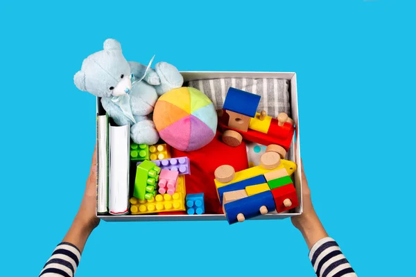 Adománykoncepció. Gyerek kéz adomány doboz ruhák, könyvek és játékok világoskék háttér. Felülnézet — Stock Fotó