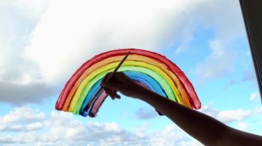 Covid-19 karantinası sırasında pencereye renkli gökkuşağı çizen çocuk. Coronavirüs enfeksiyonu tehlikesi nedeniyle evde kal. Umudun sembolü. 4k