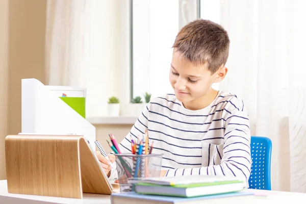 Grabben med digital surfplatta skriver, gör läxor vid bordet. Online-lärande, distansutbildning, distansundervisning hemma — Stockfoto
