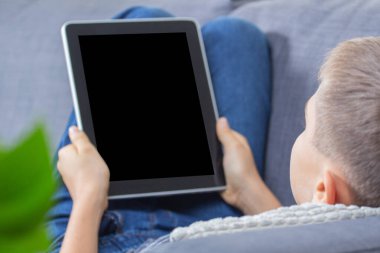 Çocuk dijital tablet bilgisayar kullanıyor ve boş ekranı evdeki kanepede gösteriyor.