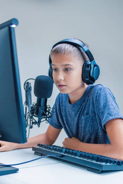 Online learning, remote education, gaming, school concept. Teenage boy talks looking to computer monitor screen. Kid wearing headphones using microphone — Stock Photo, Image