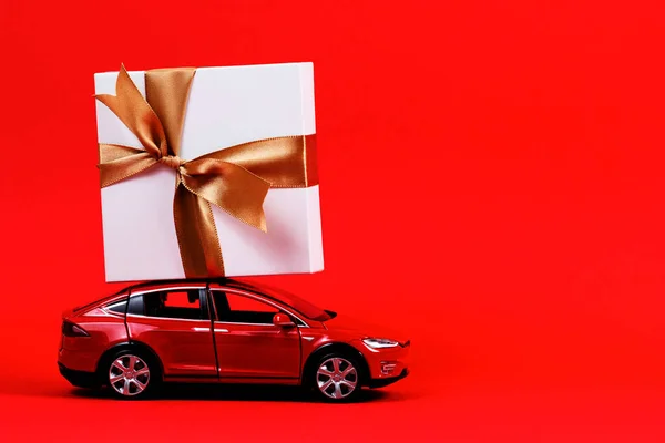 Červená hračka model auto s dárkovou krabičkou na vrcholu přes červené pozadí — Stock fotografie