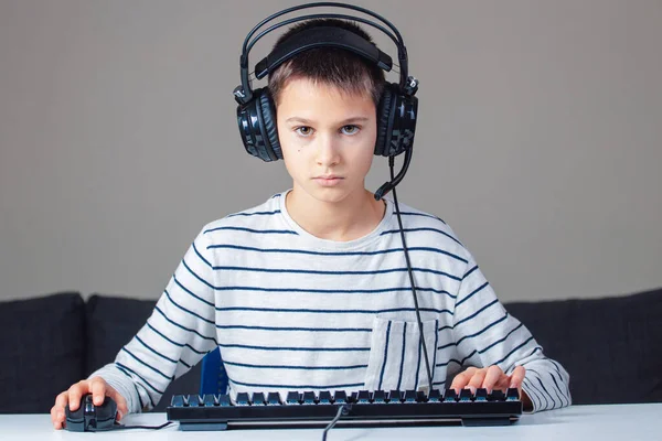 Ritratto di bambino con cuffie e tastiera seduto a casa sul computer, guardando lo schermo. — Foto Stock