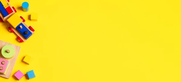 Bebé niños juguetes banner fondo. Tren de madera, apilamiento educativo juguete rompecabezas reconocimiento de color y bloques de colores sobre fondo amarillo. Vista superior — Foto de Stock