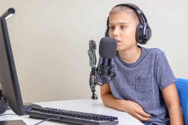 Kulaklık takan bir genç mikrofon kullanarak konuşuyor. Çocuk podcast kaydediyor, internetten öğreniyor.