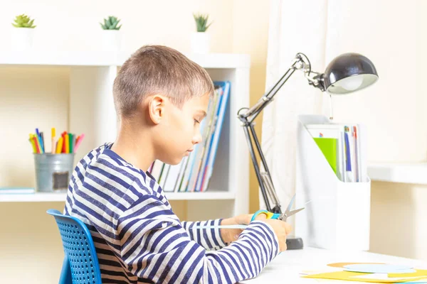 Education, learning, paper craft, entertainment. Boy cutting colored paper with scissors. Kid looking video tutorial and making paper craft project at home — Stock Photo, Image