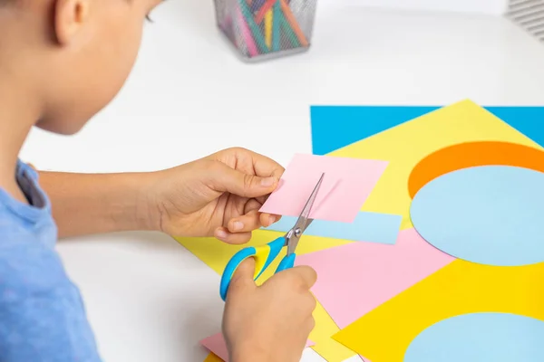 Manos de niño cortando papel de color con tijeras. Educación, aprendizaje, artesanía del papel, entretenimiento en el hogar — Foto de Stock