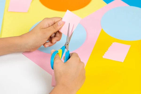 Manos de niño cortando papel de color con tijeras. Educación, aprendizaje, artesanía del papel, entretenimiento en el hogar — Foto de Stock
