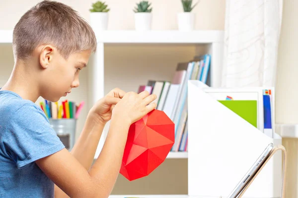 Rapaz a fazer papel vermelho poligonal coração. Educação, aprendizagem, artesanato de papel, entretenimento em casa — Fotografia de Stock