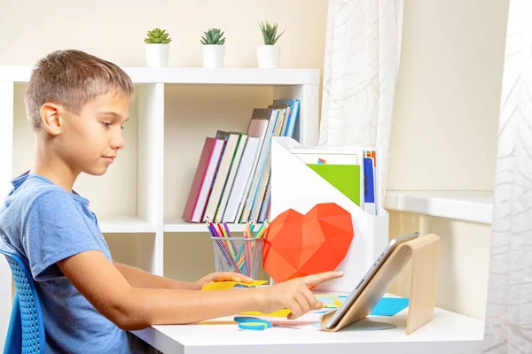 Educação, aprendizagem, artesanato de papel, entretenimento. Adolescente cortando papel colorido com tesoura. Criança procurando vídeo tutorial e fazendo projeto de ofício de papel em casa — Fotografia de Stock