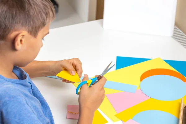 Mãos de criança cortando papel colorido com tesoura. Educação, aprendizagem, artesanato de papel, entretenimento em casa — Fotografia de Stock