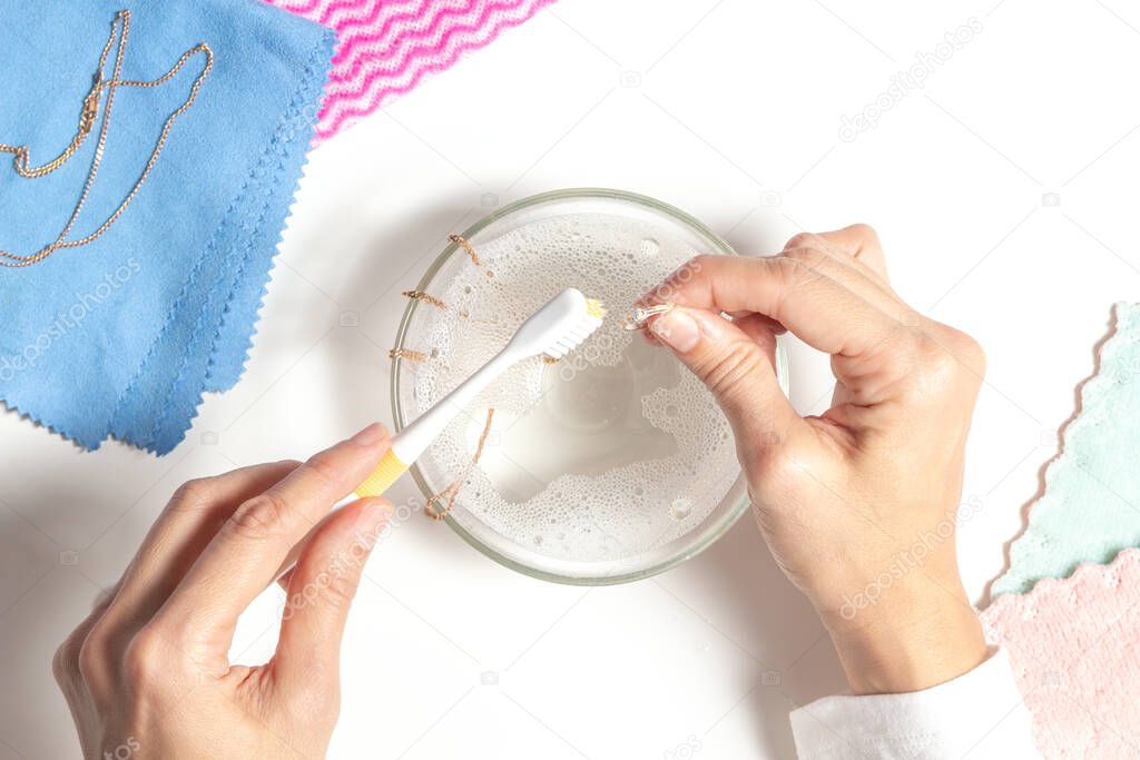 Woman hands cleaning golden jewelry at home. Top view