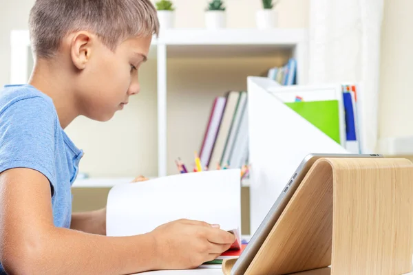 デジタルタブレットコンピュータを搭載した10代の少年は、ビデオ通話のレッスンを受け、テーブルで宿題をしています。オンライン学習、遠隔教育、自宅での遠隔授業 — ストック写真