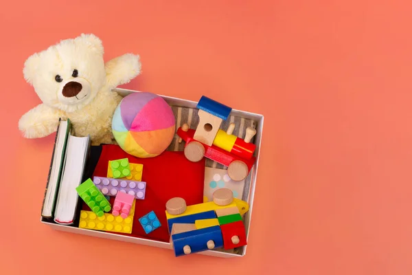 Donation box with toys, books, clothing for charity on pink background. Top view