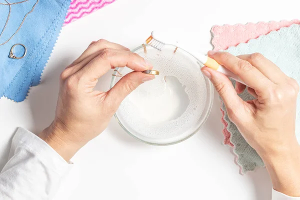 Woman hands cleaning golden jewelry at home. Top view