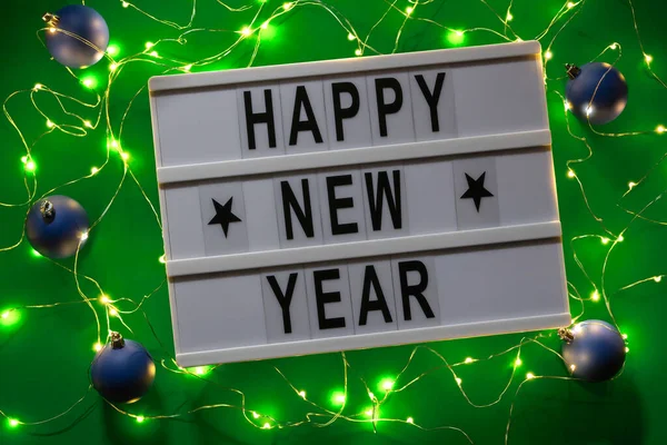 Белая буква Lightbox с поздравлениями с Новым годом, гирлянды и украшения безделушки на зеленом фоне. Вид сверху — стоковое фото