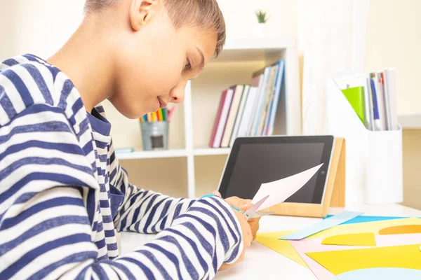 Educação, aprendizagem, artesanato de papel, entretenimento. Adolescente cortando papel colorido com tesoura. Criança procurando vídeo tutorial e fazendo projeto de ofício de papel em casa — Fotografia de Stock