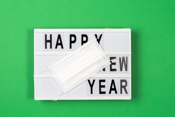Коробка с текстом HAPPY NEW YEAR с медицинской маской на зеленом фоне. Новый год во время пандемии коронавируса. Вид сверху — стоковое фото