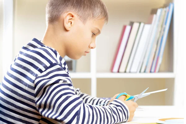 Educação, aprendizagem, artesanato de papel, entretenimento. Menino de corte de papel colorido com tesoura e fazer projeto de artesanato de papel em casa — Fotografia de Stock