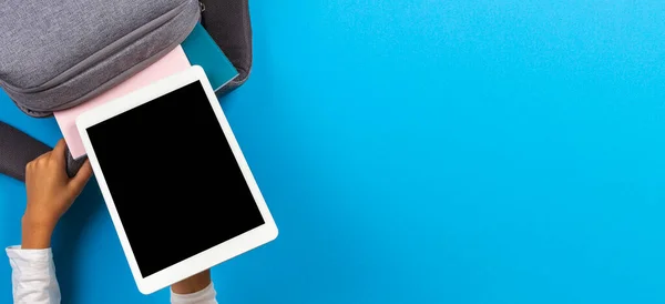 Çocuk elleri açık mavi arka planda gri sırt çantasından dijital tablet bilgisayarı alıyor. Üst görünüm — Stok fotoğraf