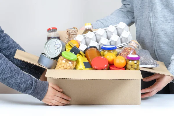 Volontärer händer som håller mat donationer låda med livsmedel produkter på vitt skrivbord — Stockfoto