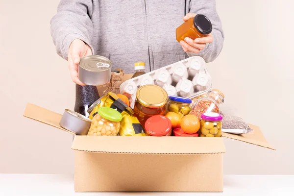 Frivilliga händer med mat donationslåda full av livsmedelsprodukter på vitt skrivbord — Stockfoto