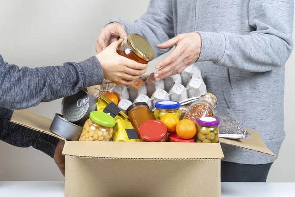 Voluntarios manos poniendo productos de comestibles, alimentos a la caja de donaciones de alimentos — Foto de Stock