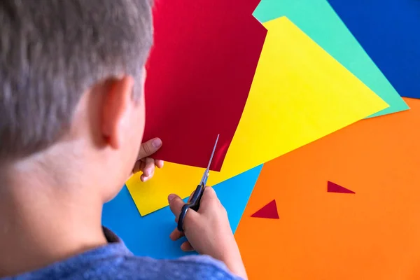 Artesanato de papel para crianças. Mãos de criança cortando papel colorido com tesoura na mesa — Fotografia de Stock