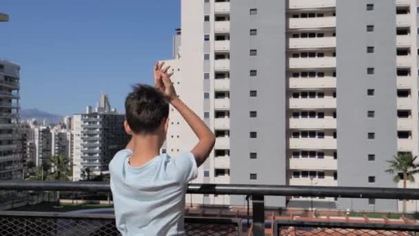Хлопчик аплодував медичним працівникам з балкона. Люди плескають балкони і вікна на підтримку працівників охорони здоров'я під час пандемії Коронавірусу. — стокове відео