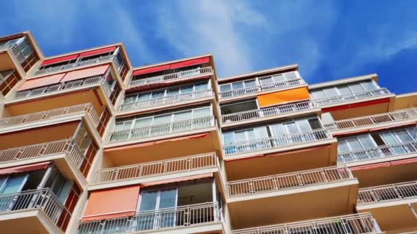 スペインの晴れた日に青い空に対して風によって静かに移動し、古いアパートの建物のバルコニーと窓への低角度ビュー — ストック動画