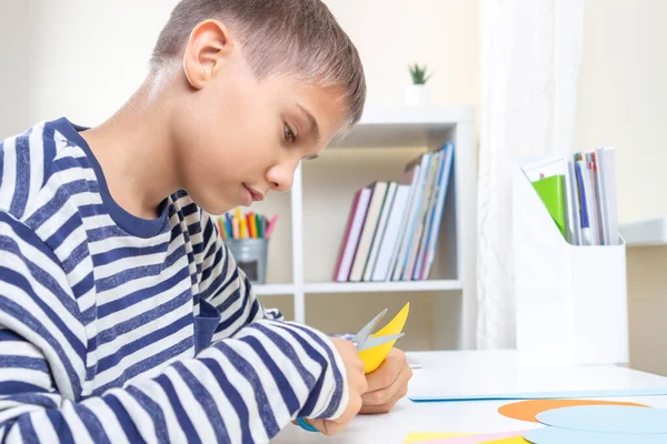 Niño cortando papel de color con tijeras y haciendo proyecto de artesanía de papel en casa. Educación, aprendizaje, artesanía del papel, entretenimiento. — Foto de Stock