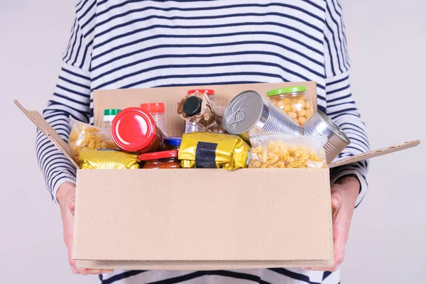 Frivilliga händer håller mat donationer låda med livsmedel produkter på vitt skrivbord — Stockfoto