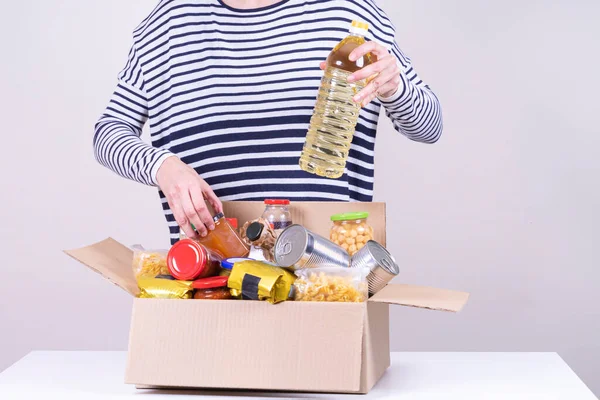 Dobrovolnické ruce držící dárcovství potravin box s potravinami produkty na bílém stole — Stock fotografie