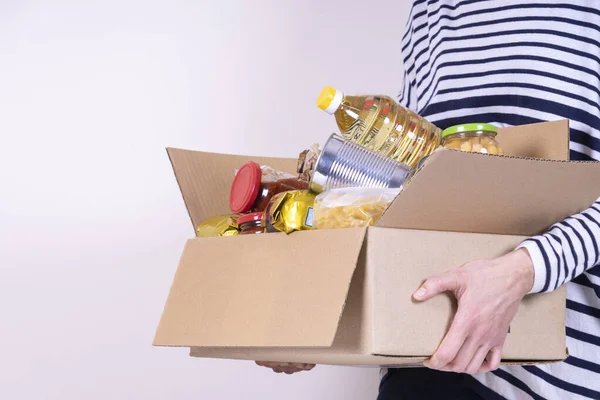 Manos voluntarias sosteniendo caja de donaciones de alimentos con productos de comestibles en escritorio blanco —  Fotos de Stock