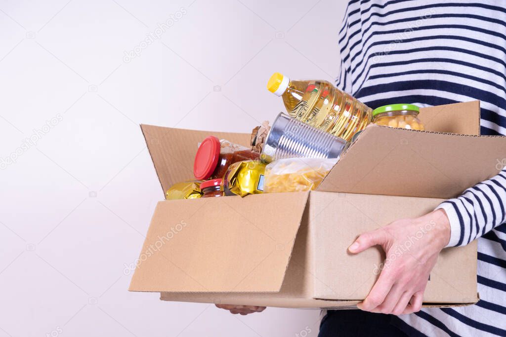 Volunteer hands holding food donations box with grocery products on white desk