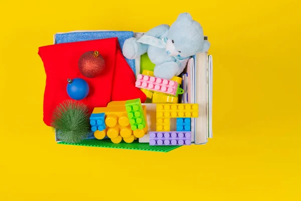 Рождественская коробка с детскими игрушками, книгами, одеждой для благотворительности на желтом фоне. Вид сверху — стоковое фото