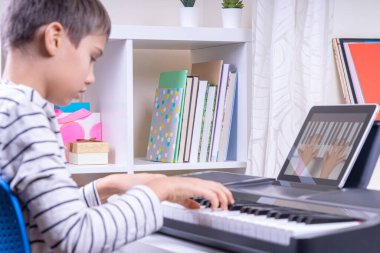 Çocuk dijital tablet bilgisayarda video dersi izliyor ve evde piyano çalıyor. Çevrimiçi öğrenim uzaktan eğitim