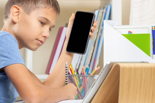 Aprendizagem online em casa. Rapaz segurando smartphone, olhando para computador tablet digital e escrever notas ou lição de casa — Fotografia de Stock