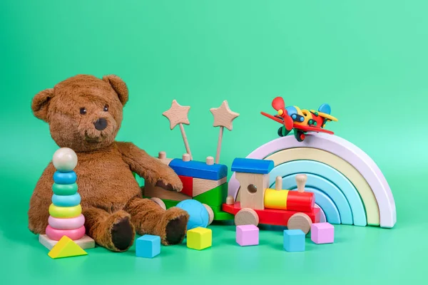 Kids toys collection. Teddy bear, wooden rainbow, train and baby toys on light green background