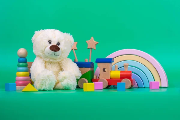 Kids toys collection. Teddy bear, wooden rainbow, train and baby toys on light green background