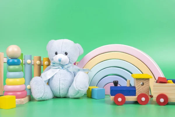 Coleção de brinquedos para crianças. Urso de pelúcia, arco-íris de madeira, trem e brinquedos de bebê no fundo verde claro — Fotografia de Stock