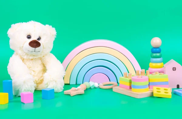 Kids toys collection. Teddy bear, wooden rainbow and baby educational toys on light green background